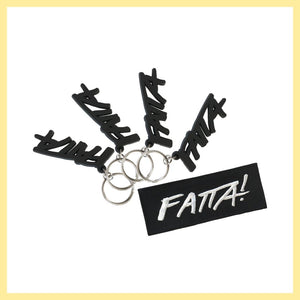 Fyra stycken nyckelringar med Fatta-loggan i mjuk svart plast och ett svart tygmärke med Fatta-loggan i vitt.